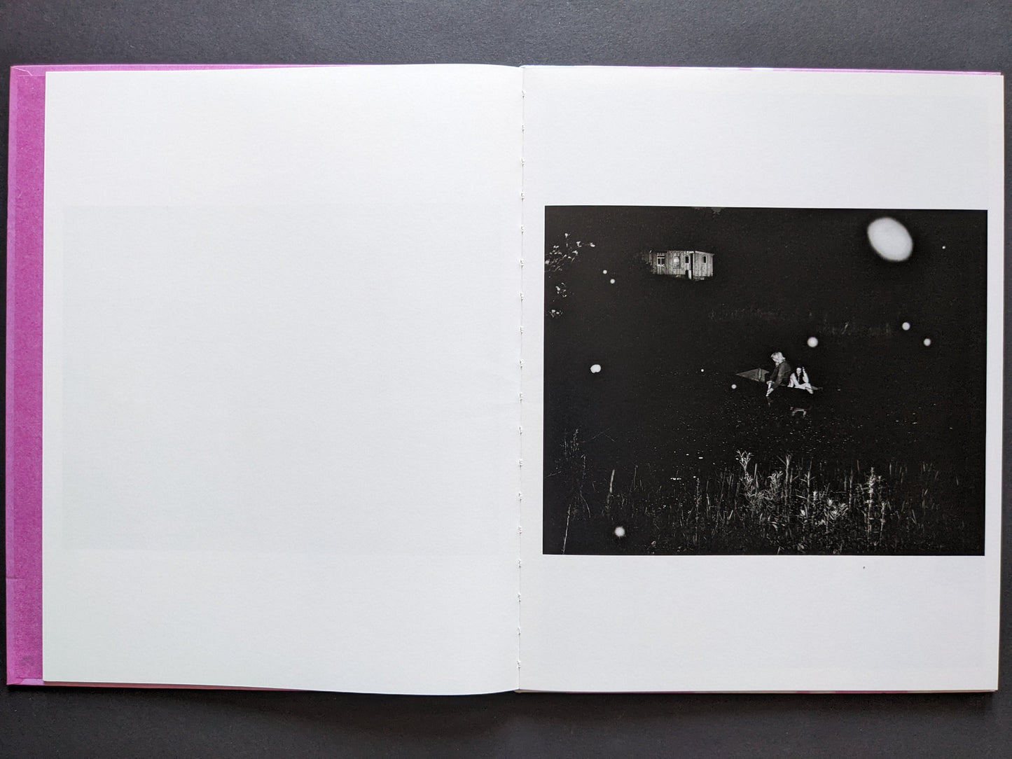 Night scene with two people in a boat, distant house, and floating white orbs in the dark, from "Flowers Drink the River."