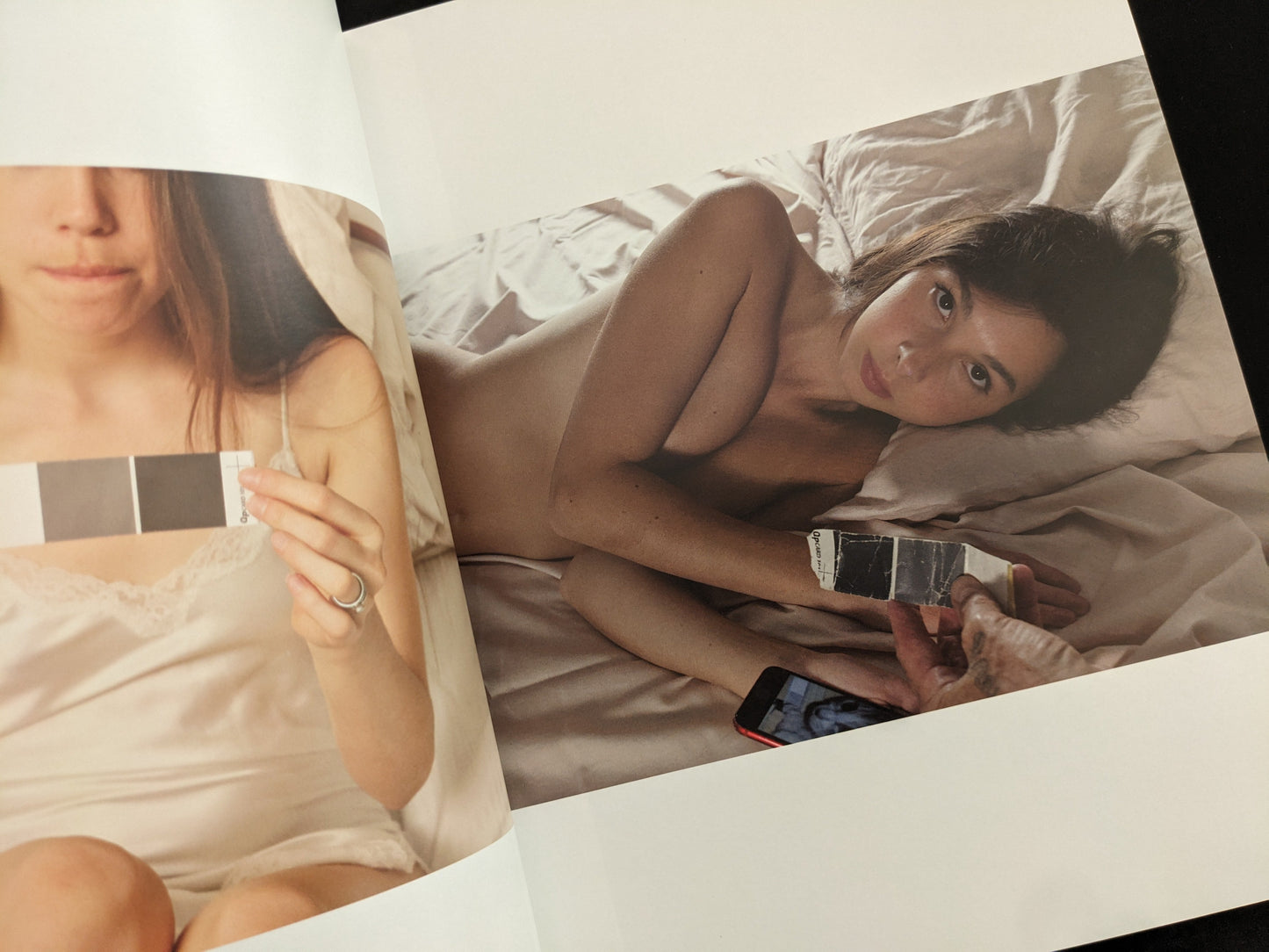 Nude portrait of a woman lying on a bed holding a grey card, from Grey Cards by Richard Kern