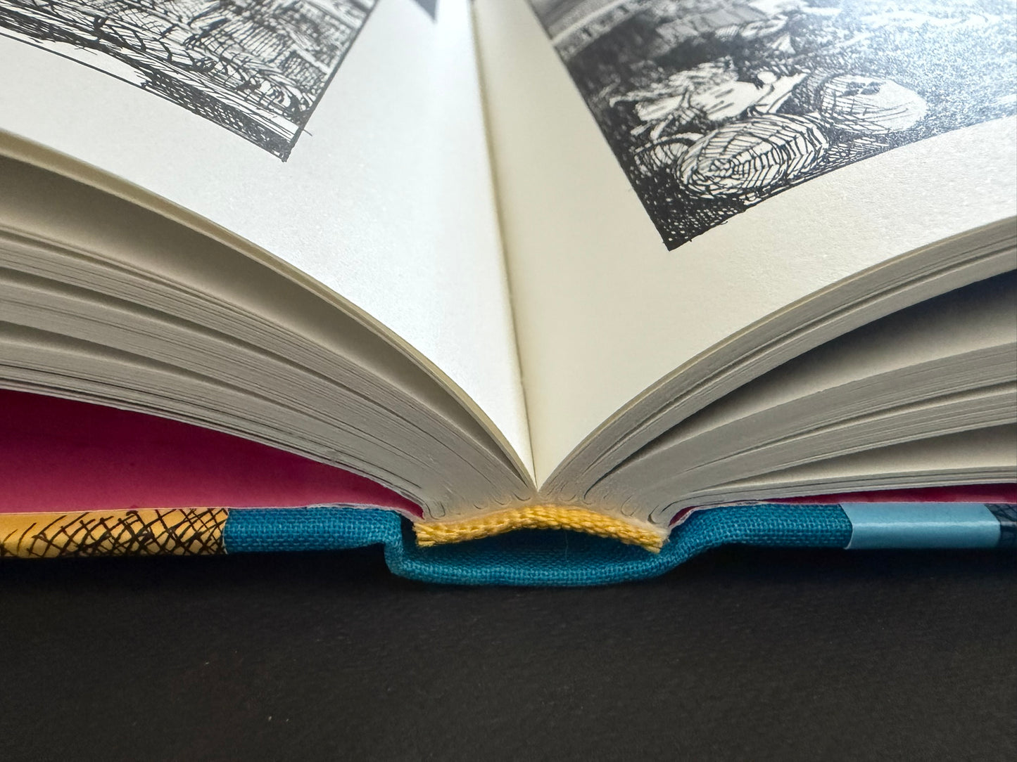Close view of GariGari opened at the gutter, showing thick page edges, the sewn binding, and part of the illustrated interior.