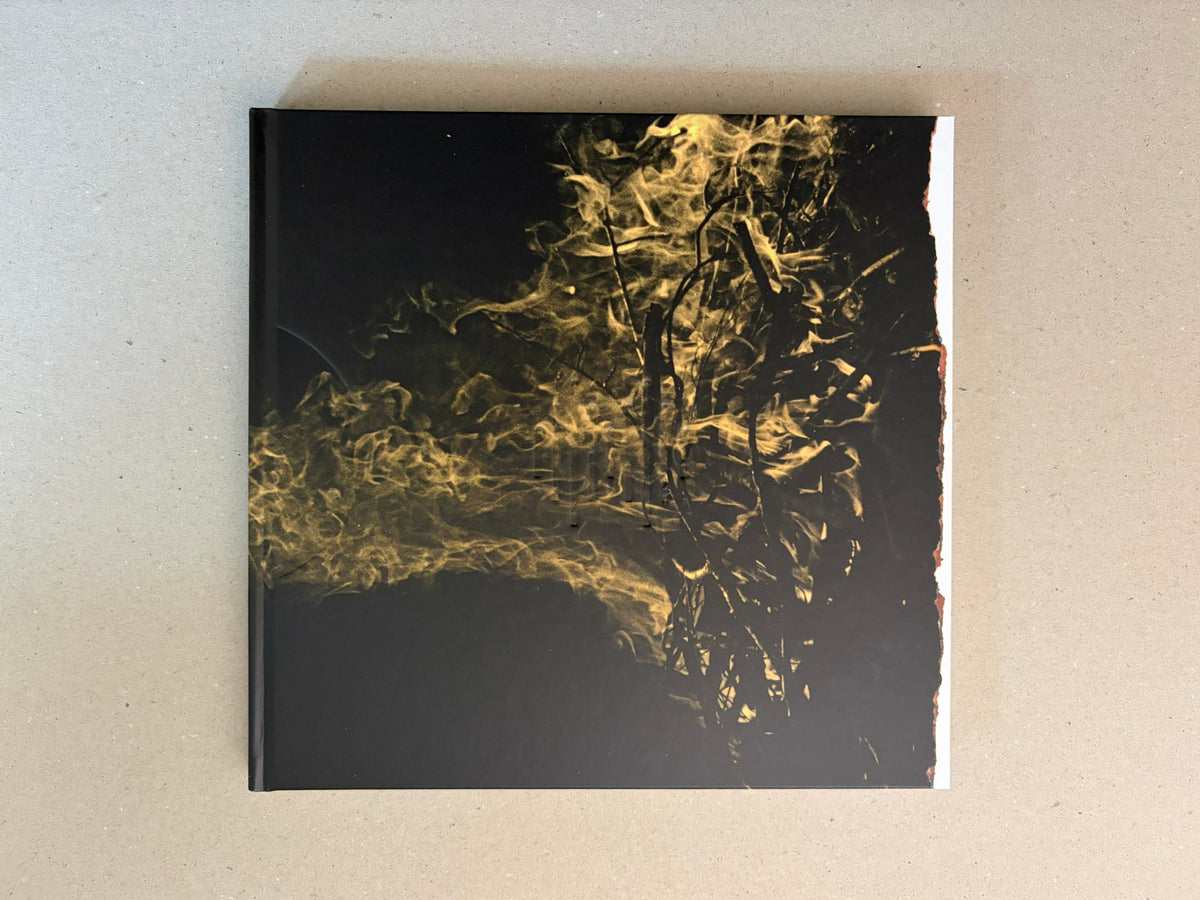 Kurayami closed and seen from above, with the black cover and gold smoke-like image centered on a grey surface.