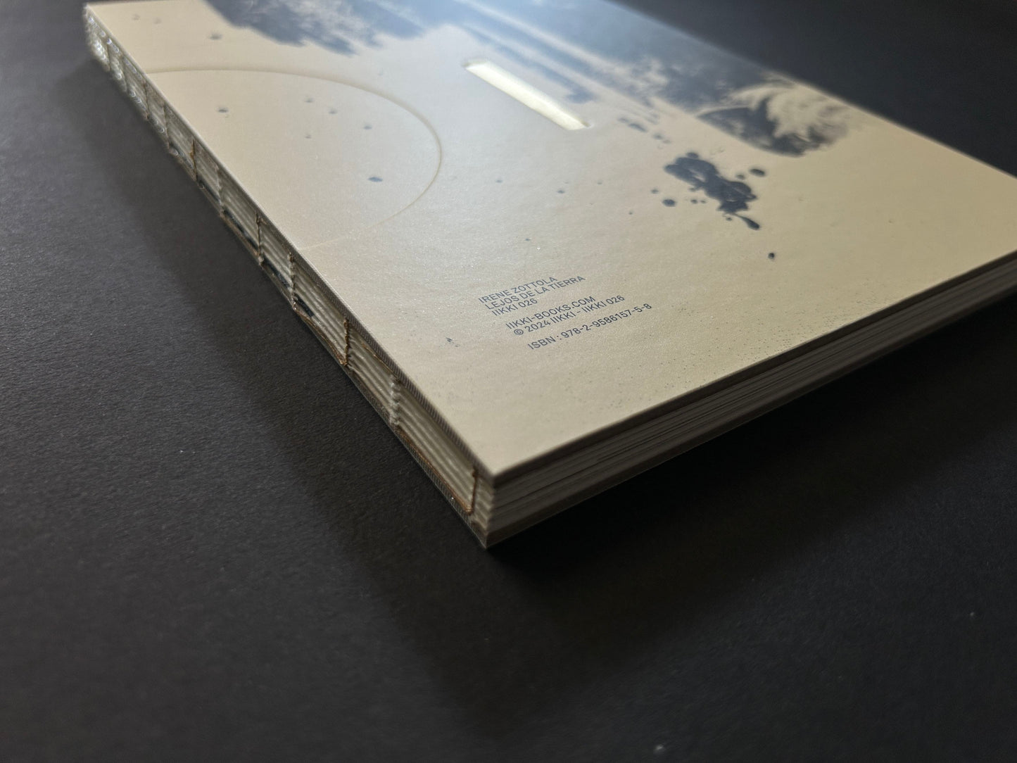 Angled view of the Lejos De La Tierra photobook showing the cover, stitched spine, and stacked page edges