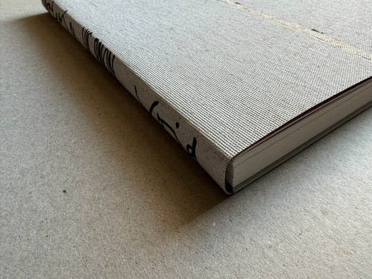 Materia by Vic Bakin, close-up of the cloth-covered hardcover book lying on a plain surface, showing the textured cover and page block at the fore edge.