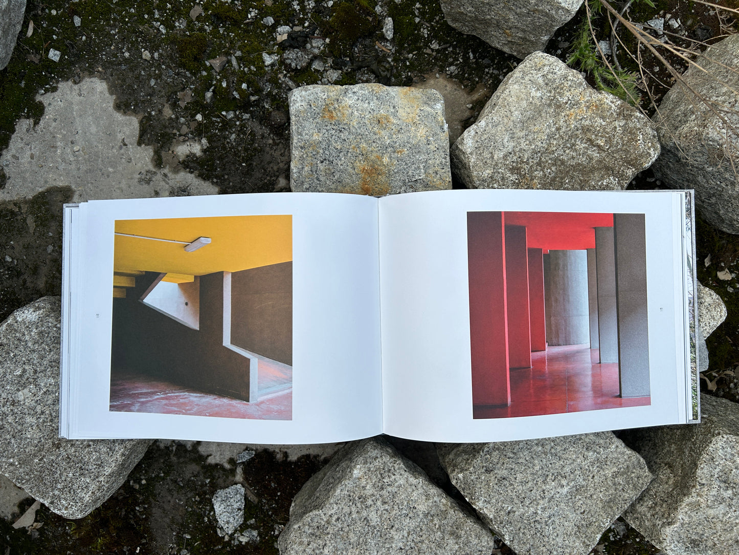 Book 'Alveare' by Matthias Heiderich and Andrea Belfi open to a spread with colorful interior architectural photography, placed on rocks IIKKI - Lokator100