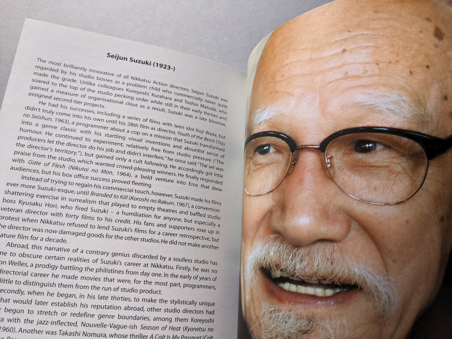 Close-up color photo of director Seijun Suzuki with biographical text on his Nikkatsu Action films.