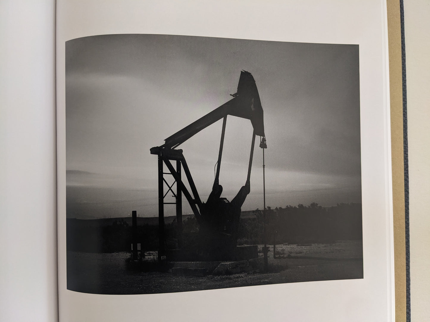 Black-and-white photograph of an oil pumpjack in the American West from No Fences by Mark McLennan