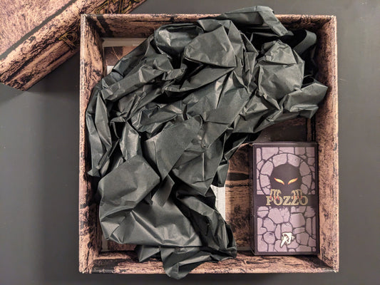 Inside view of the POZZO game box with components partially wrapped in black paper.