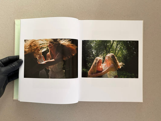 Open spread of The Virgin Suicides showing two color photographs of young women outdoors, with a gloved hand holding the book.