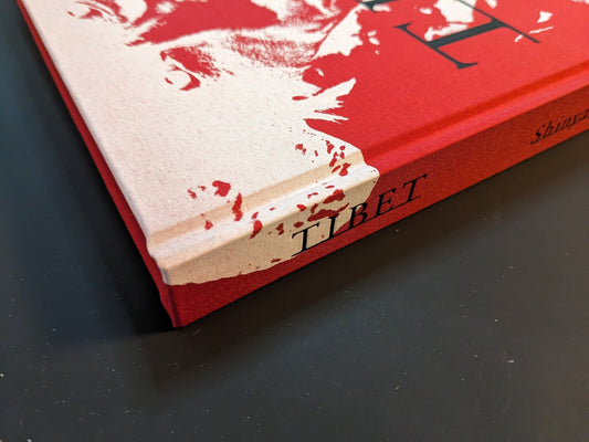 Close-up of the spine and lower corner of the photobook “TIBET” by Shinya Arimoto, highlighting the red-and-cream cloth cover and printed title.