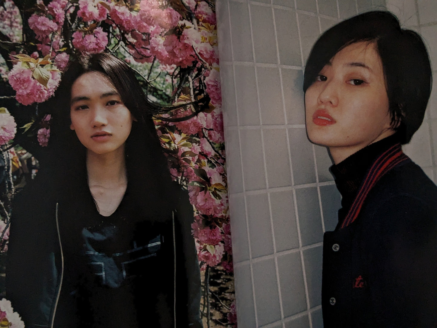 Two women standing in front of a floral curtain and tiled wall.