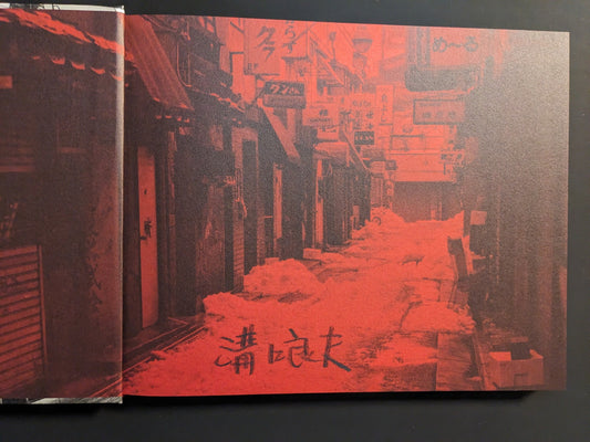 Red-toned endpaper spread with a Tokyo side street, shop signs, and snow-covered roofs in grainy halftone.