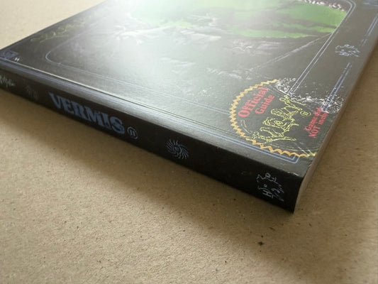 Vermis II – Mist & Mirrors by Plastiboo, angled view of the softcover showing the glossy cover and spine on a tabletop.