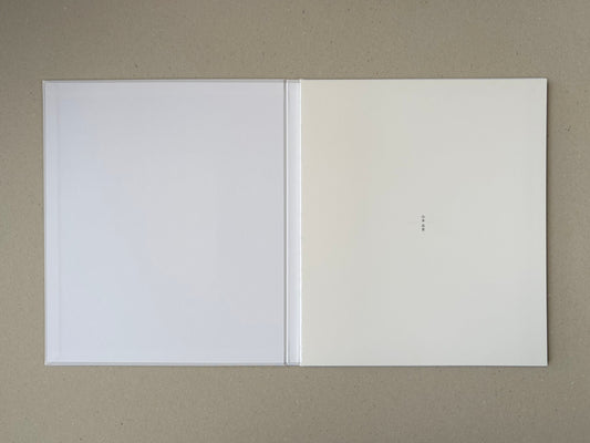 Open Yamamoto Masao photobook showing blank white endpapers and a small vertical Japanese title mark on the right page.