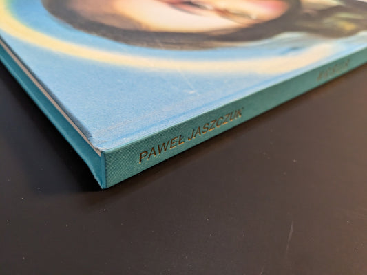 Close-up of the spine of the photobook “¥€$U$ (JESUS)” by Pawel Jaszczuk, with the author’s name stamped in gold on turquoise cloth.