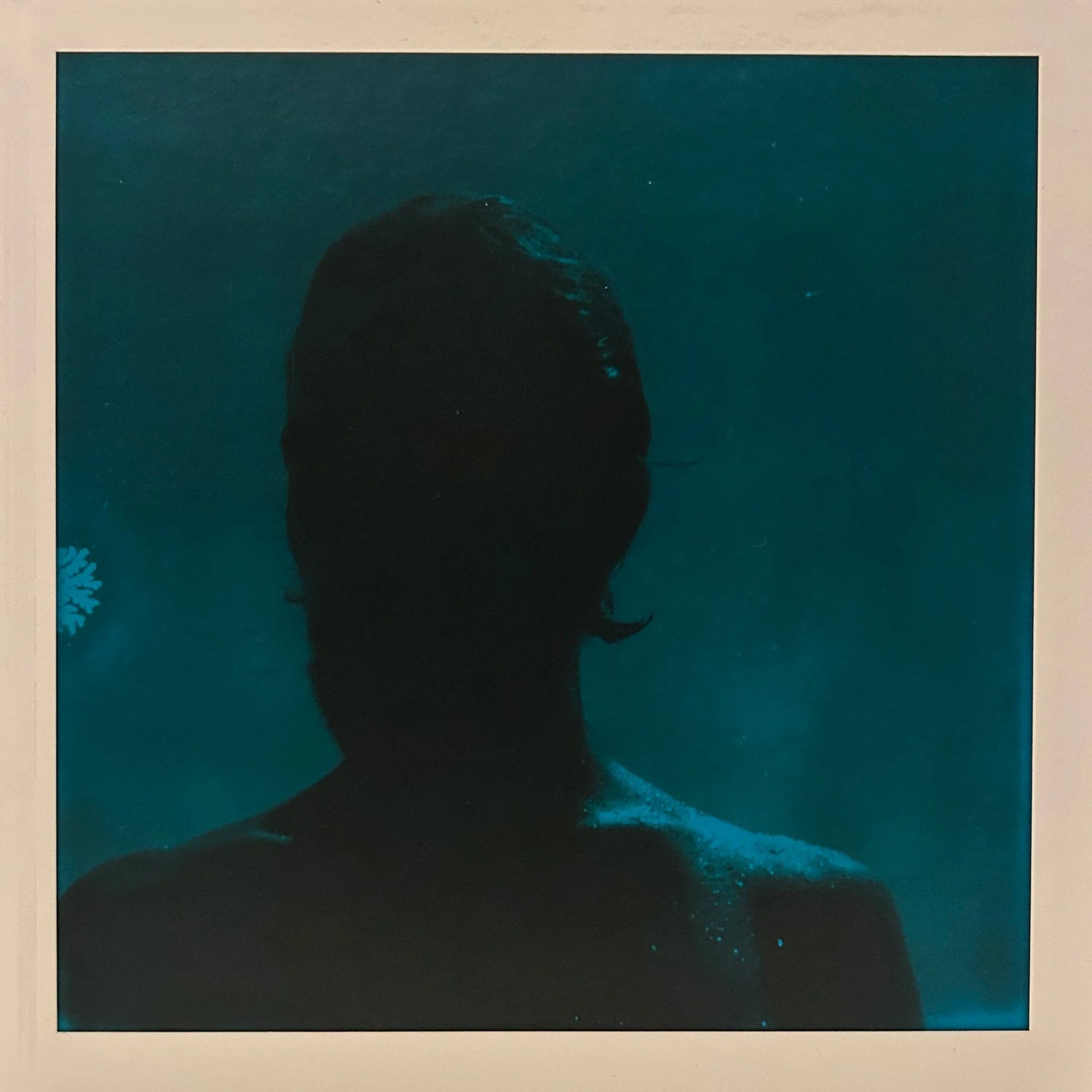 Blue-green underwater portrait of a person seen from behind, with the head and shoulders in silhouette.
