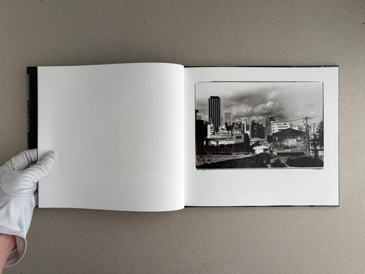 Open spread of 1980s Remnants by Daido Moriyama, showing a black-and-white cityscape photograph on the right page and a blank left page.