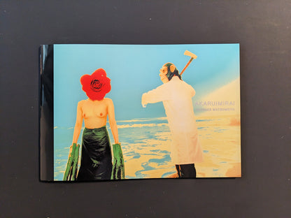 Cover of the photobook “AKARUIMIRAI” by Daisuke Matsumoto showing a topless woman with a red flower head and a man in a white coat standing on the beach in saturated colours.