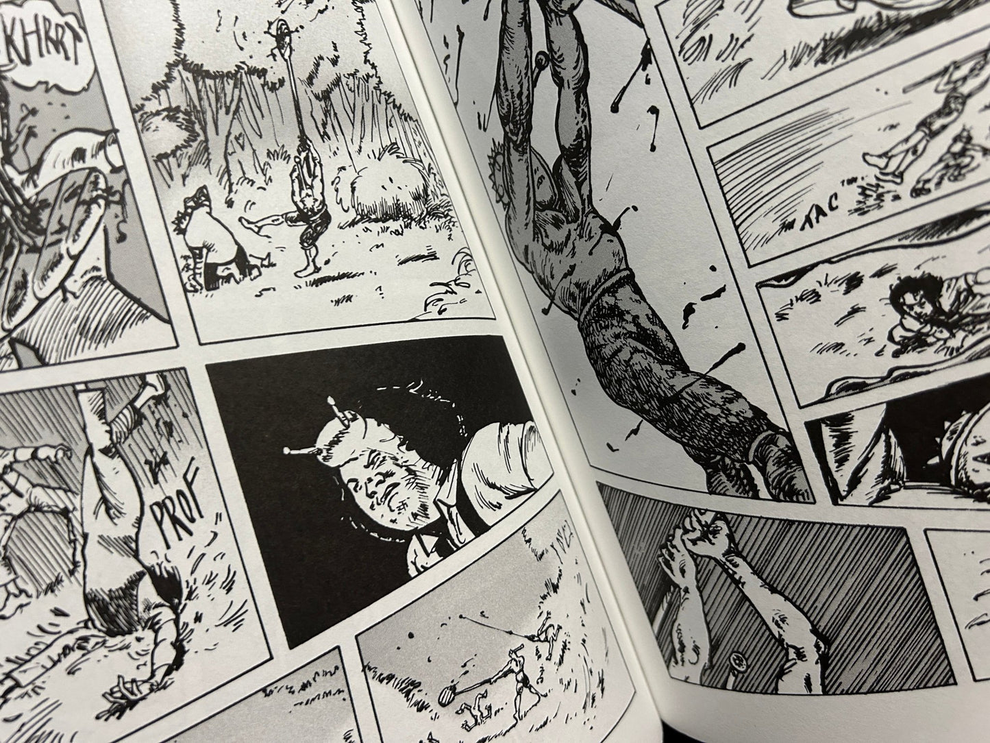 Close view of an open comic spread with dense black-and-white linework, figures in action, and multiple panels across both pages.