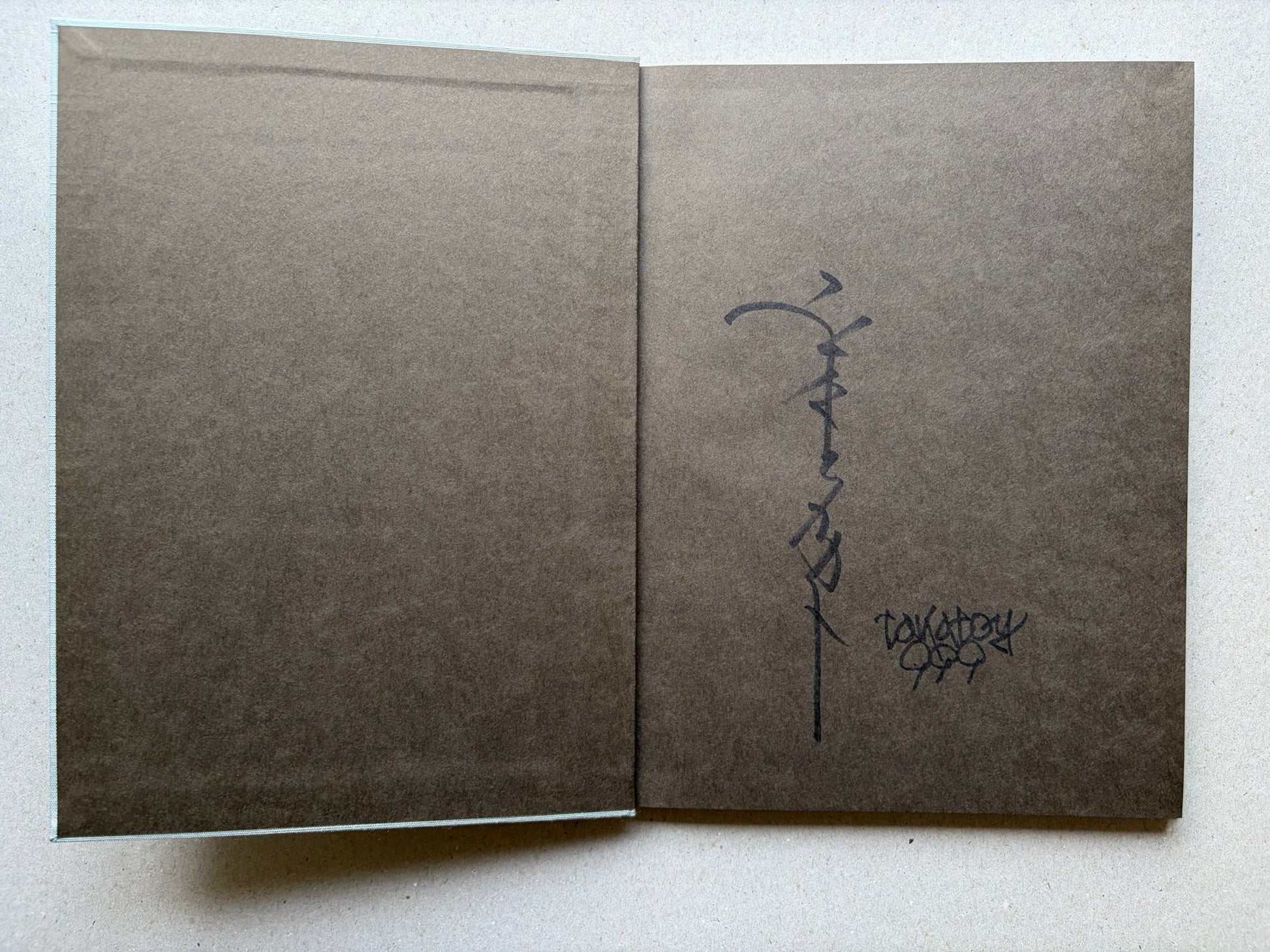 Allure of Pharmakon by Takato Yamamoto, charcoal grey endpapers with signed page spread
