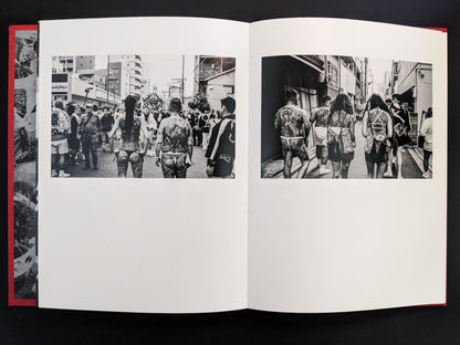 Black-and-white photo of tattooed men walking during a festival
