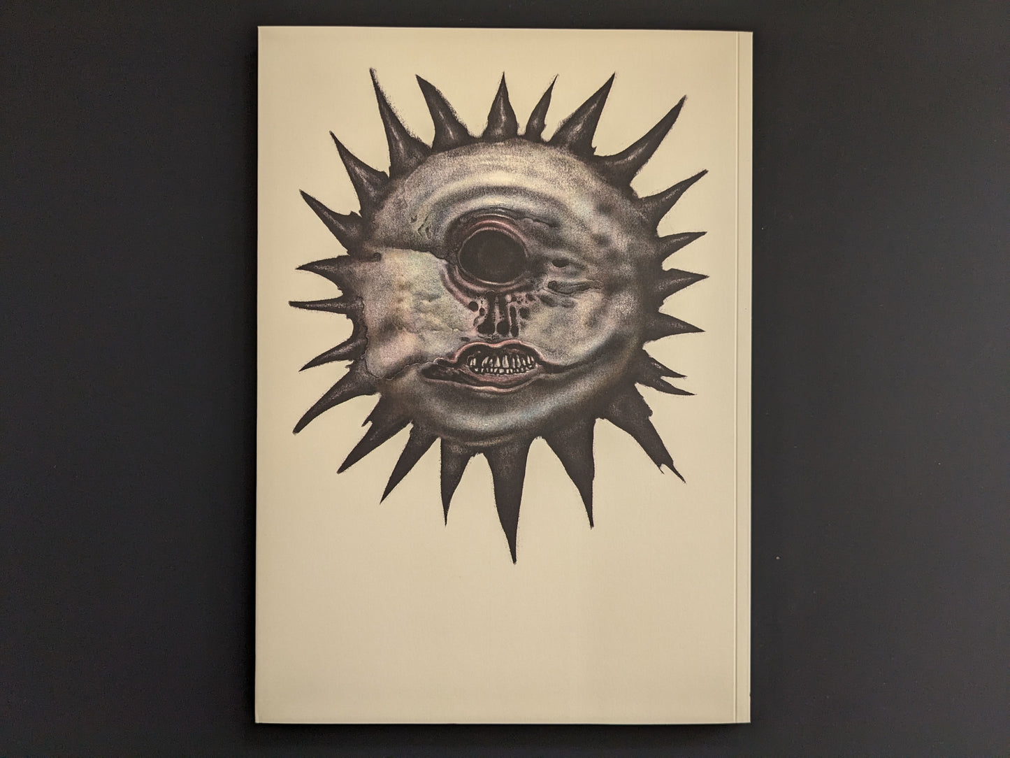 Back cover with a spiked sun-like face centered on a plain light background.