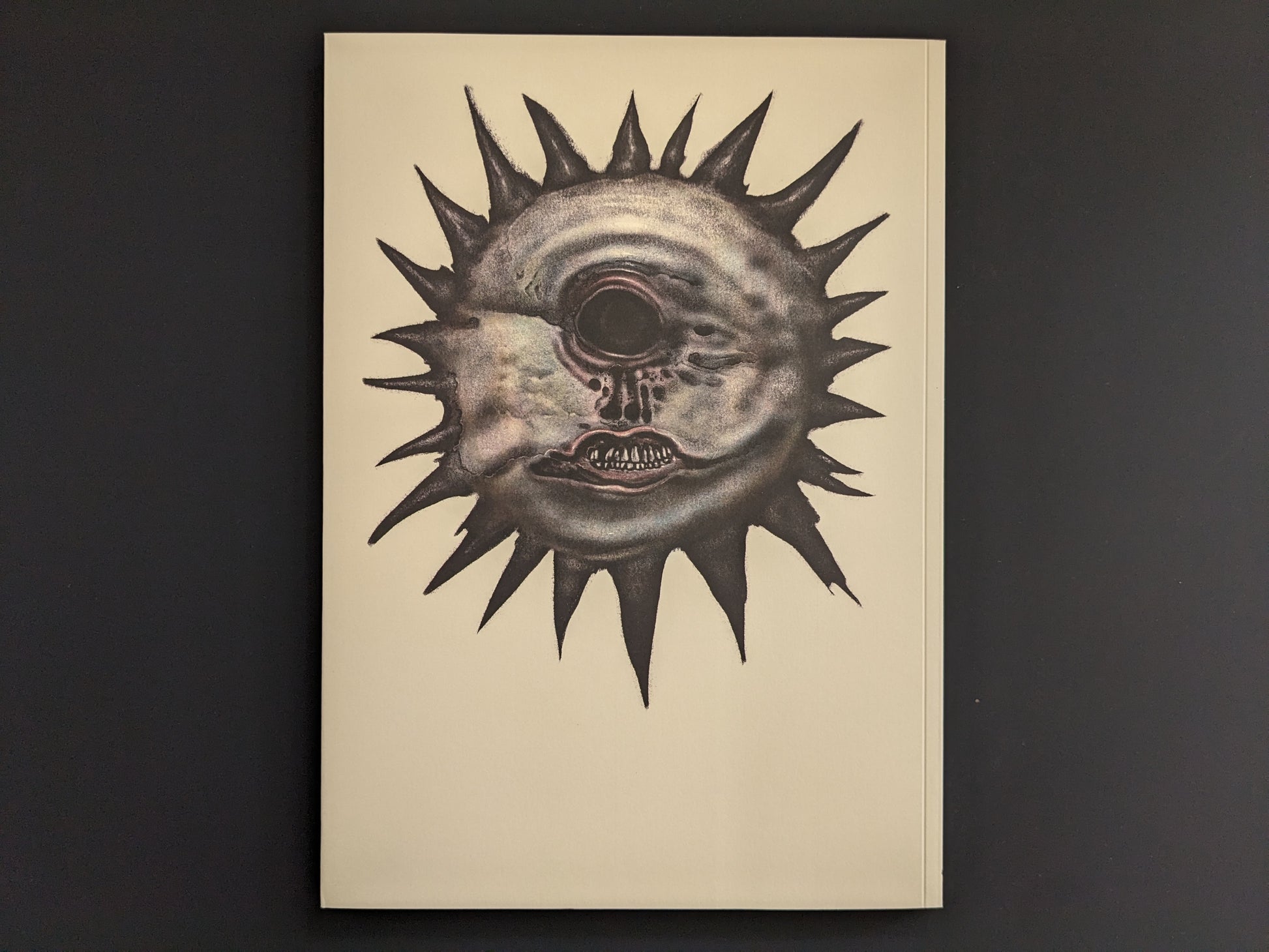 Back cover with a spiked sun-like face centered on a plain light background.
