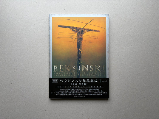 Beksiński - The Collected Works I ver. 1.2 front cover on a grey surface, with an orange painting and the title printed across the lower half.