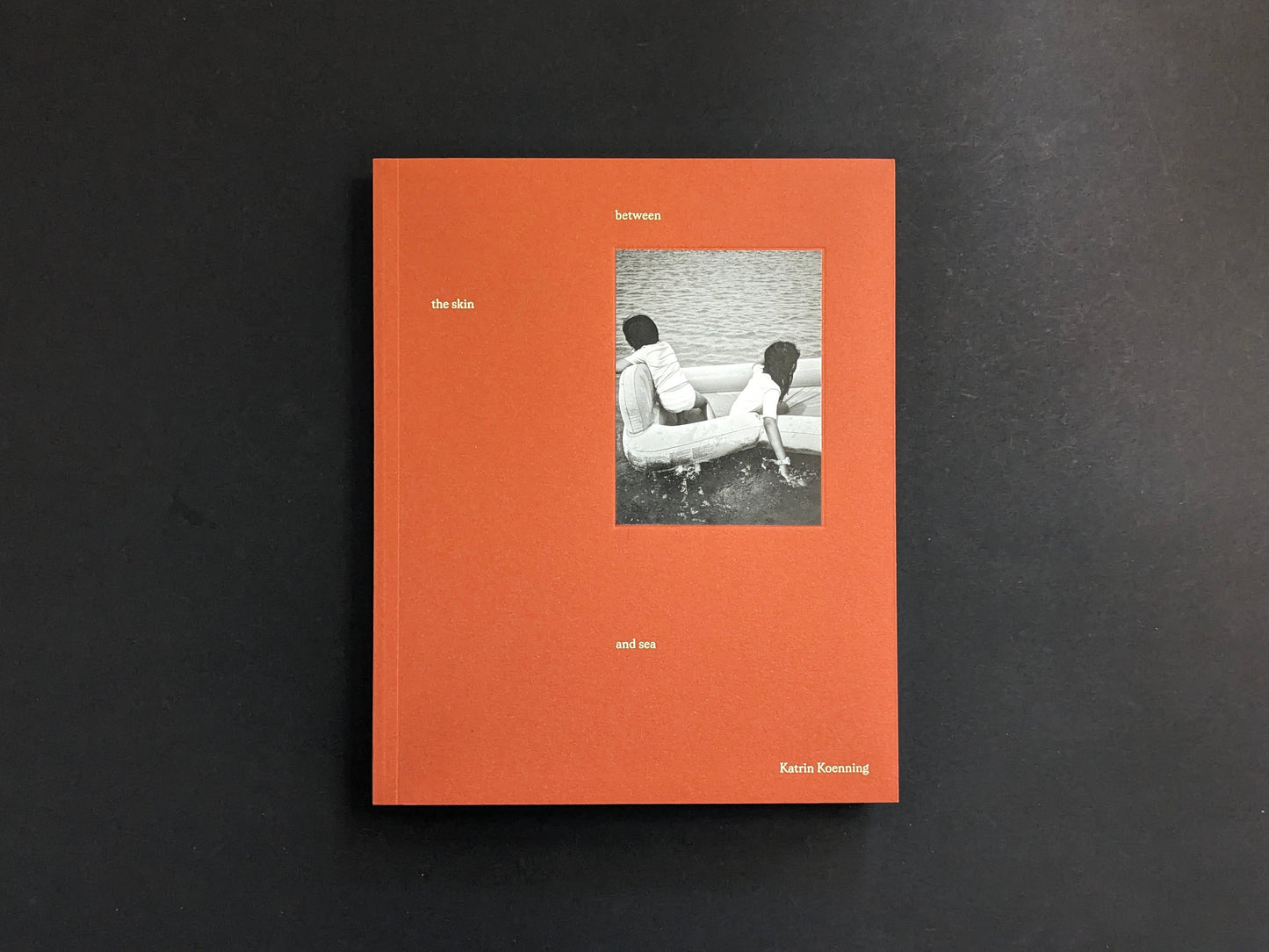 Front cover of between the skin and sea by Katrin Koenning (Chose Commune), orange softcover with a small black-and-white photo inset.