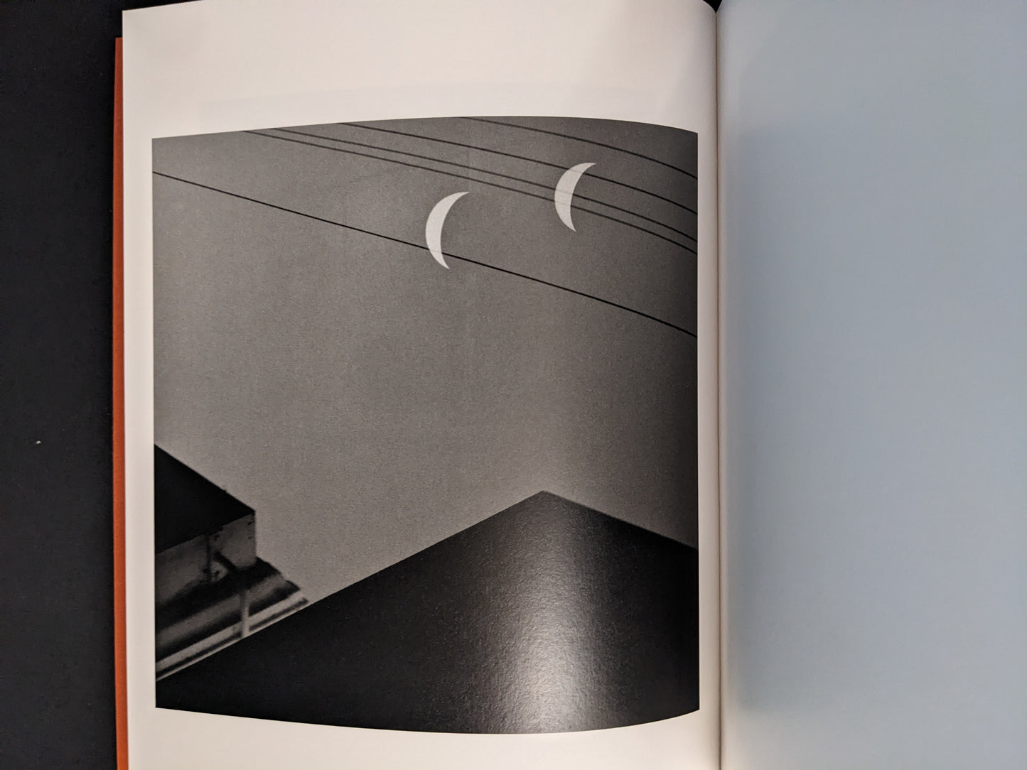 Interior photograph from “between the skin and sea” by Katrin Koenning: two crescent shapes above power lines, black-and-white.