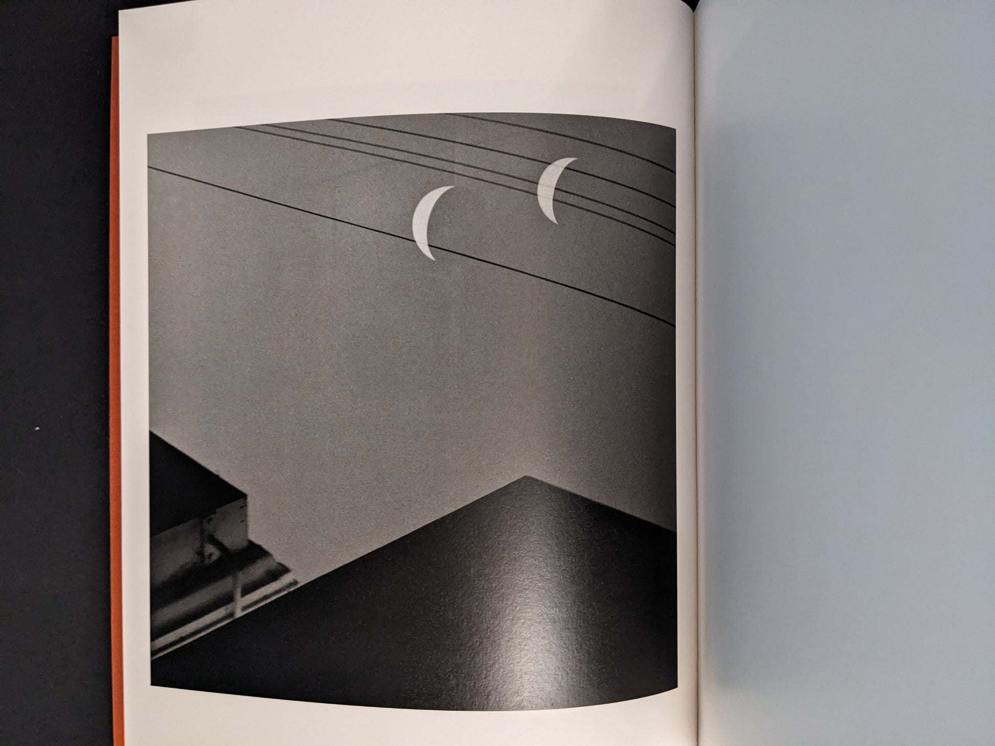 Interior photograph from “between the skin and sea” by Katrin Koenning: two crescent shapes above power lines, black-and-white.