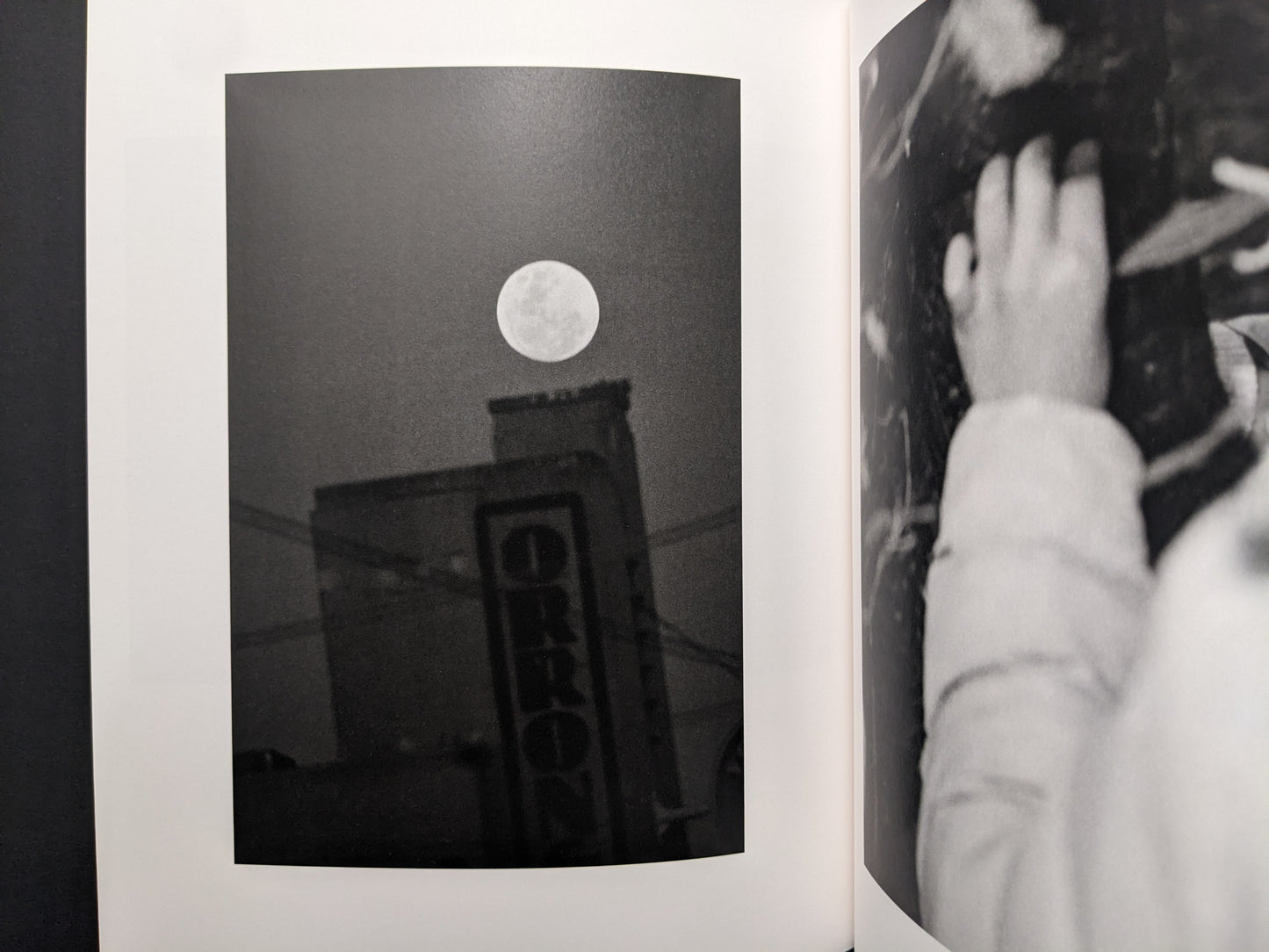 Interior photograph from “between the skin and sea” by Katrin Koenning: full moon above a building sign, black-and-white.