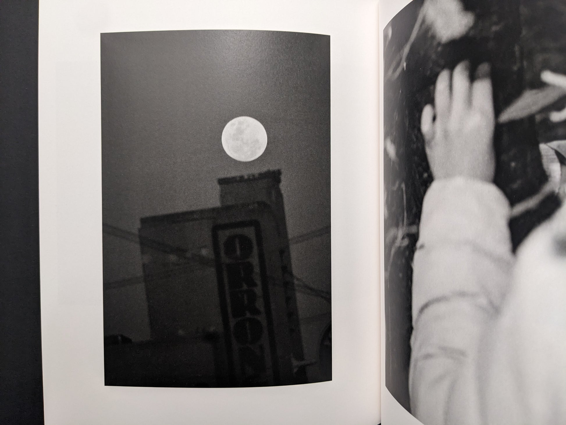 Interior photograph from “between the skin and sea” by Katrin Koenning: full moon above a building sign, black-and-white.