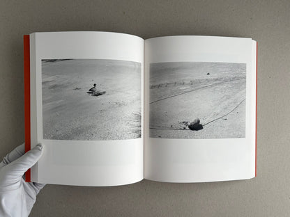 Open spread of between the skin and sea by Katrin Koenning, showing two black-and-white photographs of a shoreline with small objects and lines in the sand.