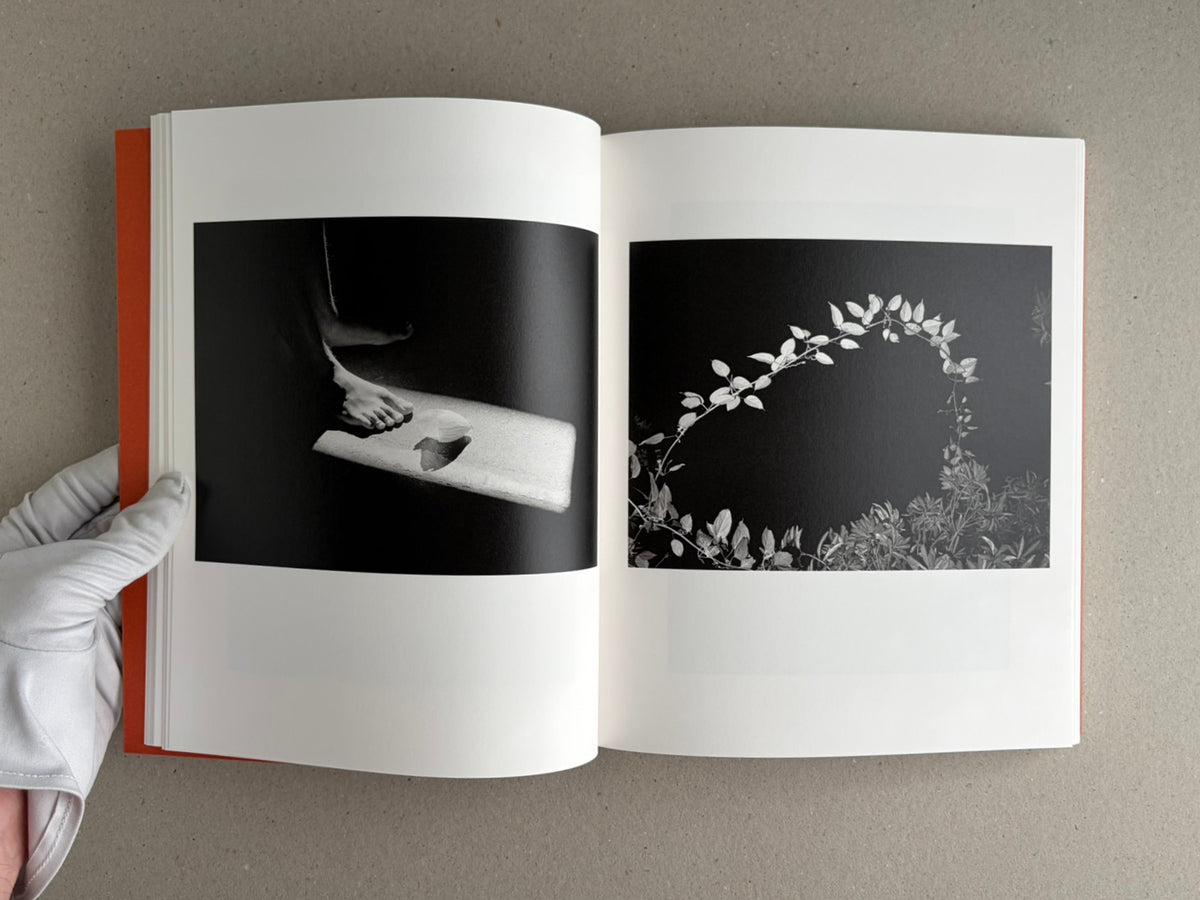 Open spread from between the skin and sea by Katrin Koenning, showing two black-and-white photographs on facing pages: a foot on a ledge at left and a curved branch of leaves at right.