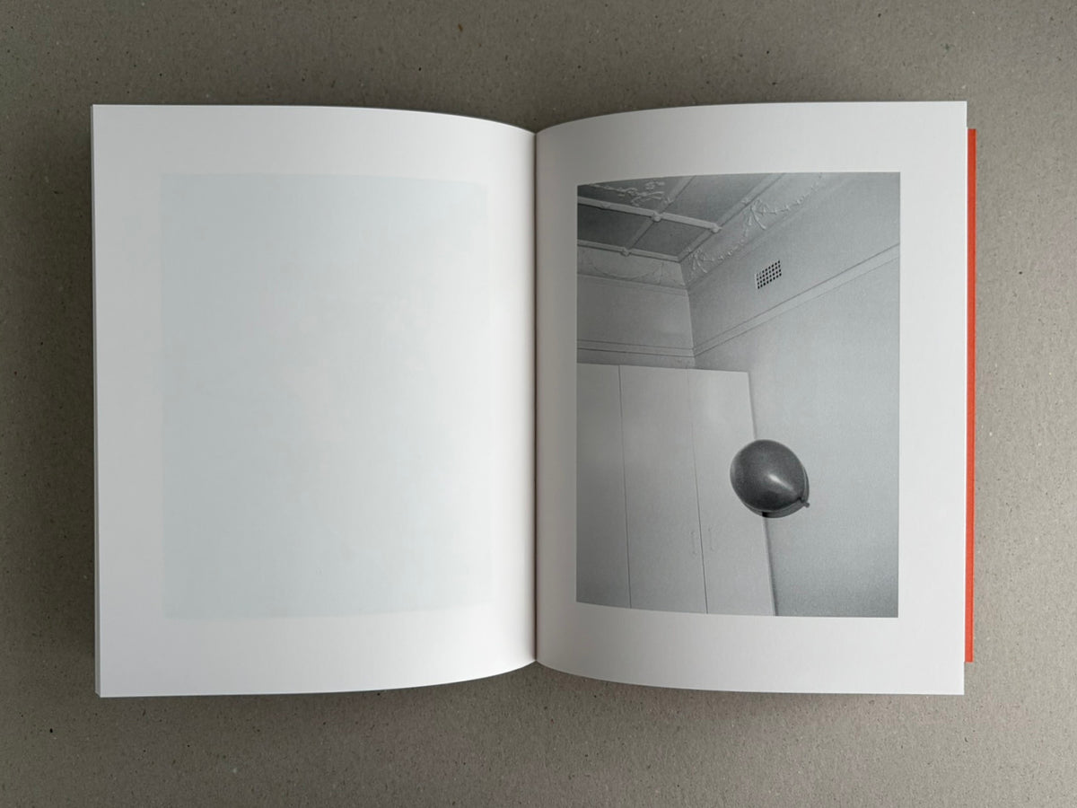 Open photobook spread from between the skin and sea by Katrin Koenning, showing a pale blank left page and a grayscale interior photograph on the right page.