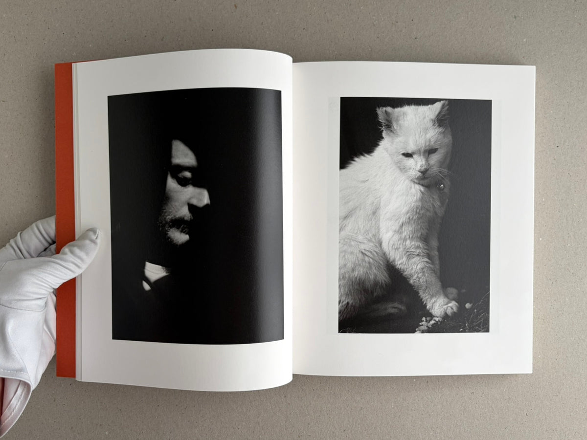 Open photobook spread from between the skin and sea by Katrin Koenning, showing a dark portrait on the left page and a black-and-white cat on the right page.