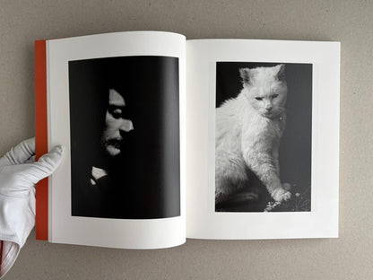 Open photobook spread from between the skin and sea by Katrin Koenning, showing a dark portrait on the left page and a black-and-white cat on the right page.