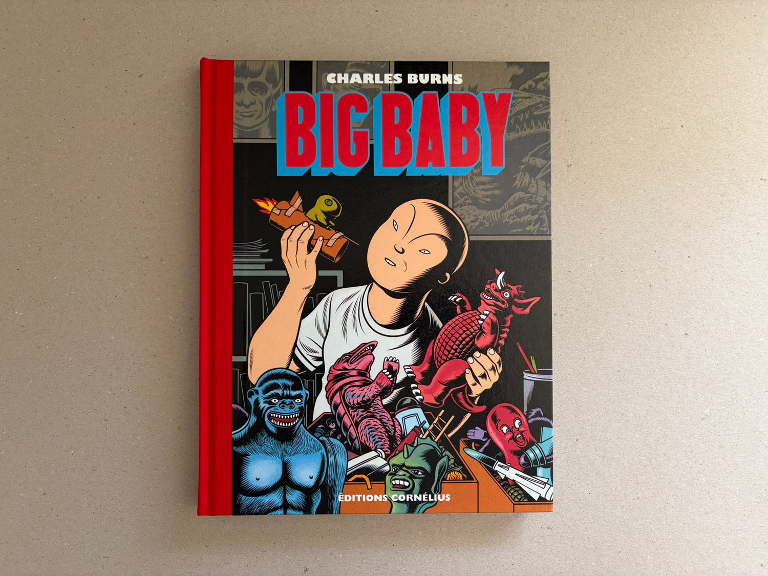 Big Baby by Charles Burns, front cover with red cloth spine and a child holding a toy against a horror-themed collage.