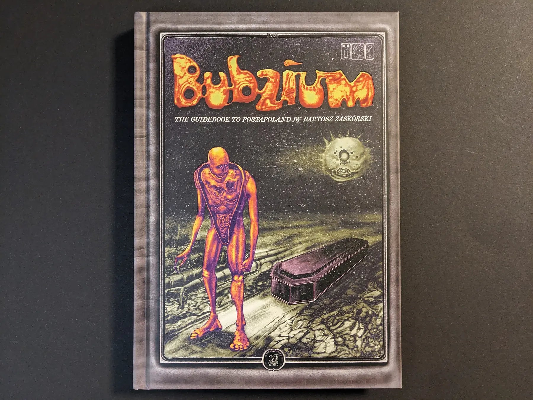 Front cover of Bubzium – the guidebook to Postapoland showing a tall orange mutant, coffin and eerie moon over a desolate landscape.