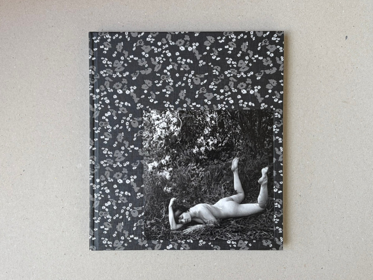 Cover of Cheryomushki by Nikolay Bakharev, showing a black-and-white photograph of a nude figure lying in grass, framed by a floral patterned border.