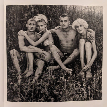 Cheryomushki by Nikolay Bakharev interior photo: black-and-white portrait of four young people sitting together in grass with arms around each other.