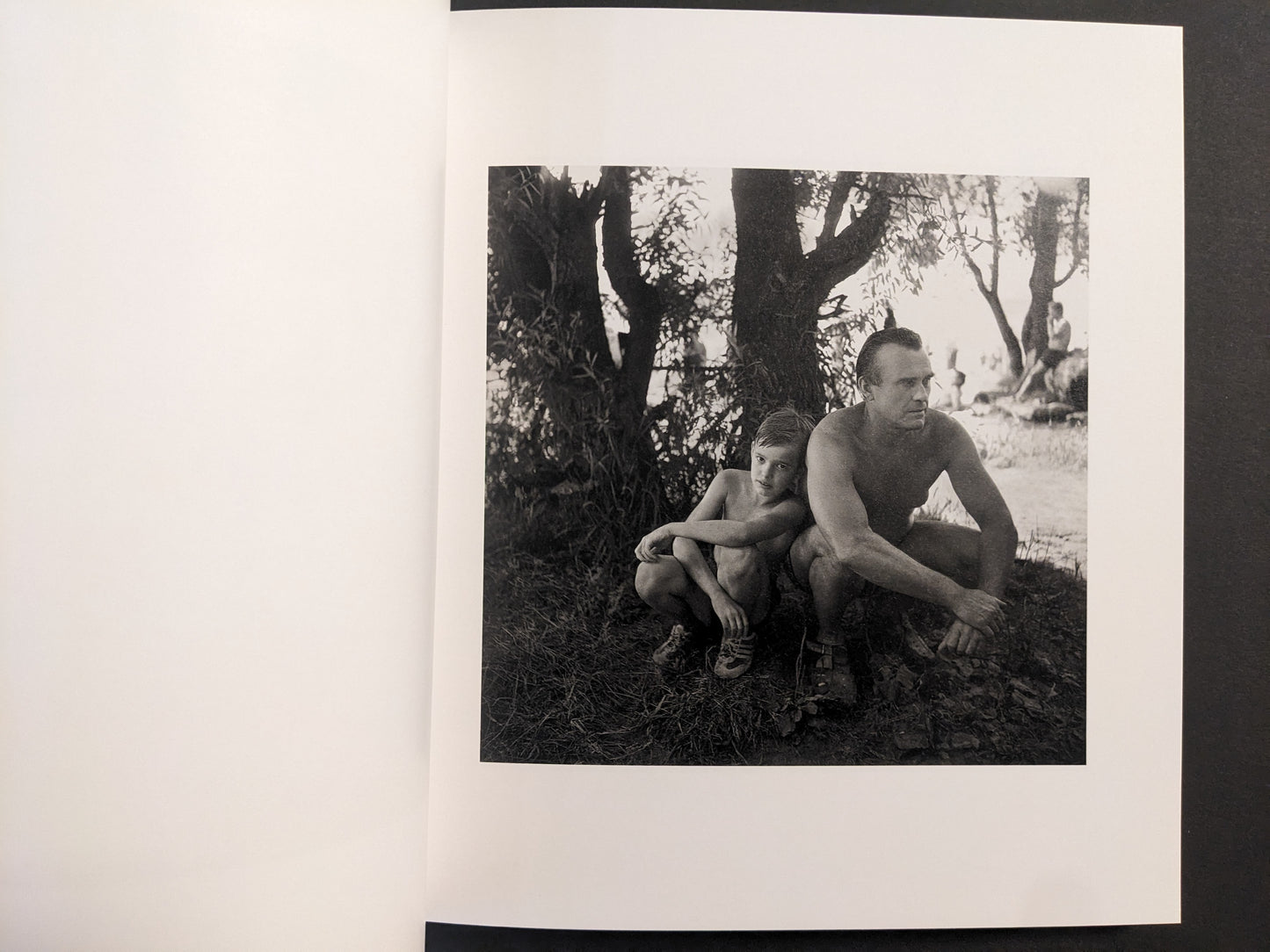 Interior photo from Cheryomushki: man and child resting under trees near a riverside beach.