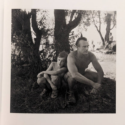 Interior photo from Cheryomushki: man and child resting under trees near a riverside beach.