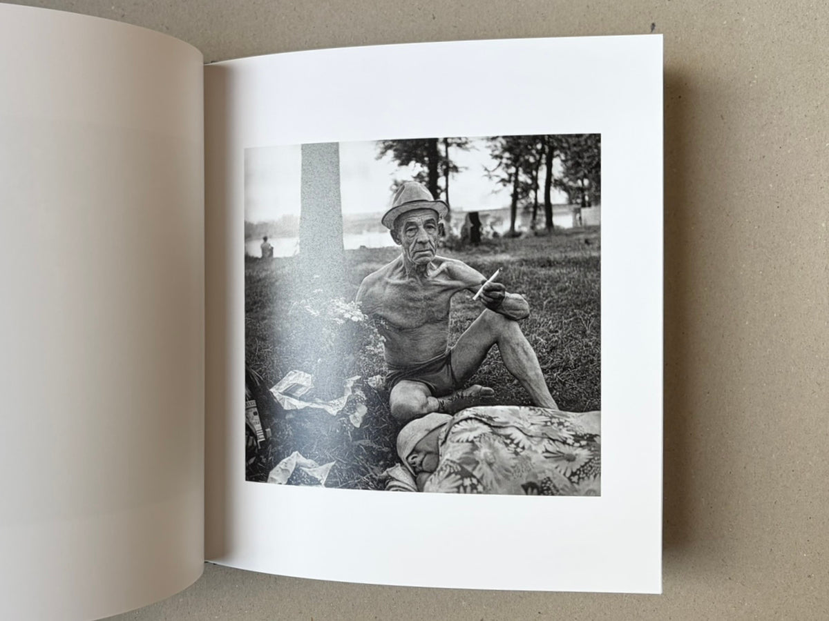 Open book page with a black-and-white photograph from Cheryomushki by Nikolay Bakharev, showing an elderly man seated outdoors near a body of water.