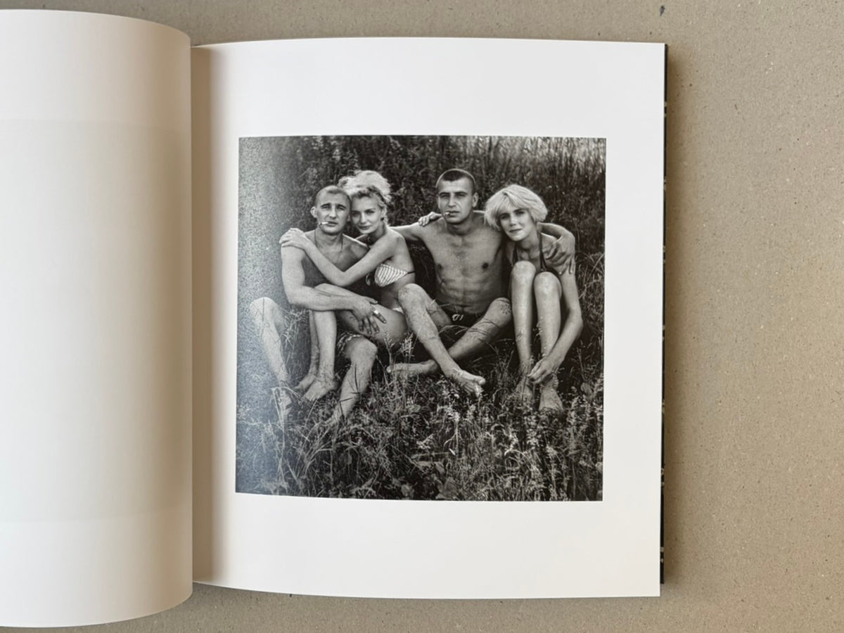 Open book page with a black-and-white photograph from Cheryomushki by Nikolay Bakharev, showing four people seated closely together in grass.