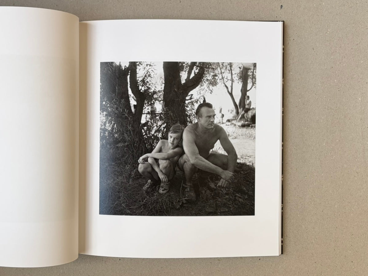 Open book page showing a black-and-white photograph from Cheryomushki by Nikolay Bakharev, with a man and child crouching beneath trees.