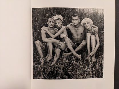 Cheryomushki by Nikolay Bakharev interior photo: black-and-white portrait of four young people sitting together in grass with arms around each other.