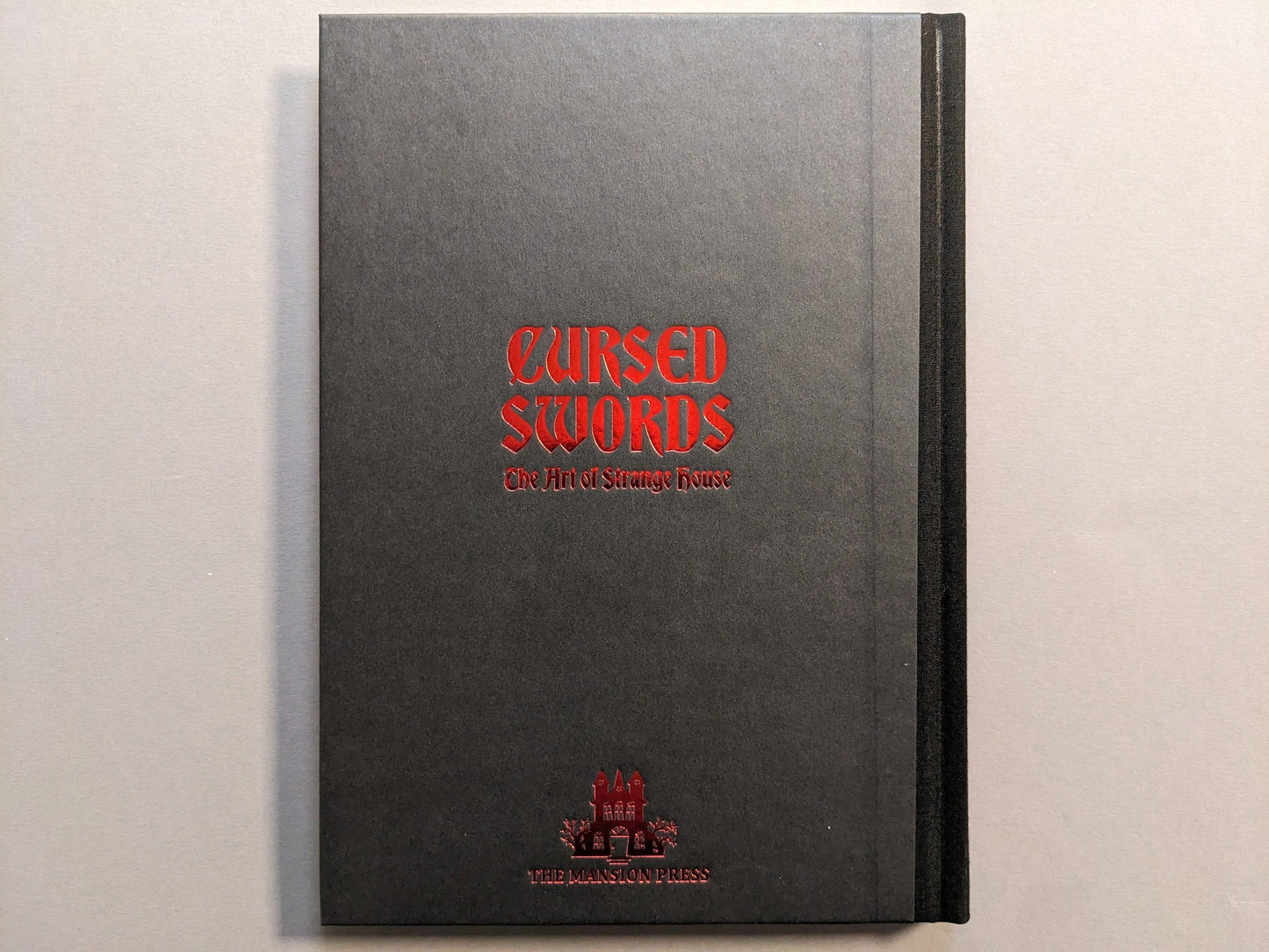 Hardcover board of Cursed Swords by Strange House / Joonas Ryynänen, cloth spine and red hot-stamped title.