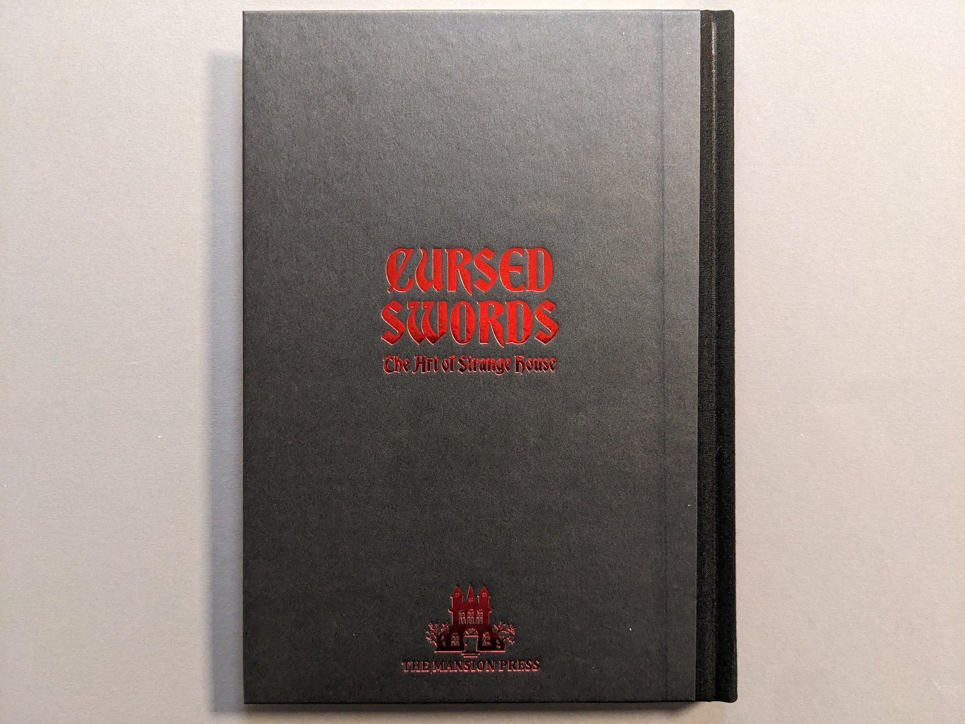 Hardcover board of Cursed Swords by Strange House / Joonas Ryynänen, cloth spine and red hot-stamped title.