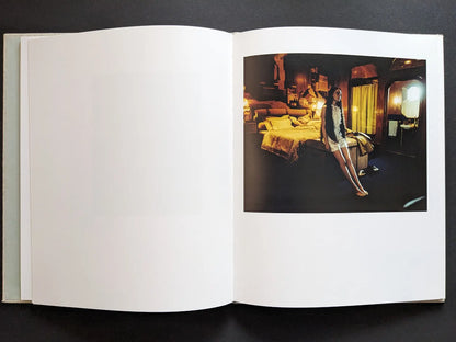 Color scene with a woman standing in a bedroom set under warm lighting.