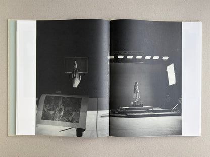 Black-and-white studio spread from Dear God, the Parthenon is still broken, with a hand holding a small figure on the left and a lit stage setup on the right.